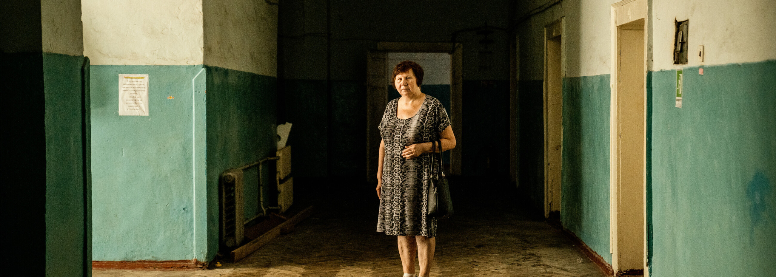 Ältere Frau steht in einem dunklen, heruntergekommenen Flur in der Ukraine – Symbol für Isolation und prekäre Wohnsituation.