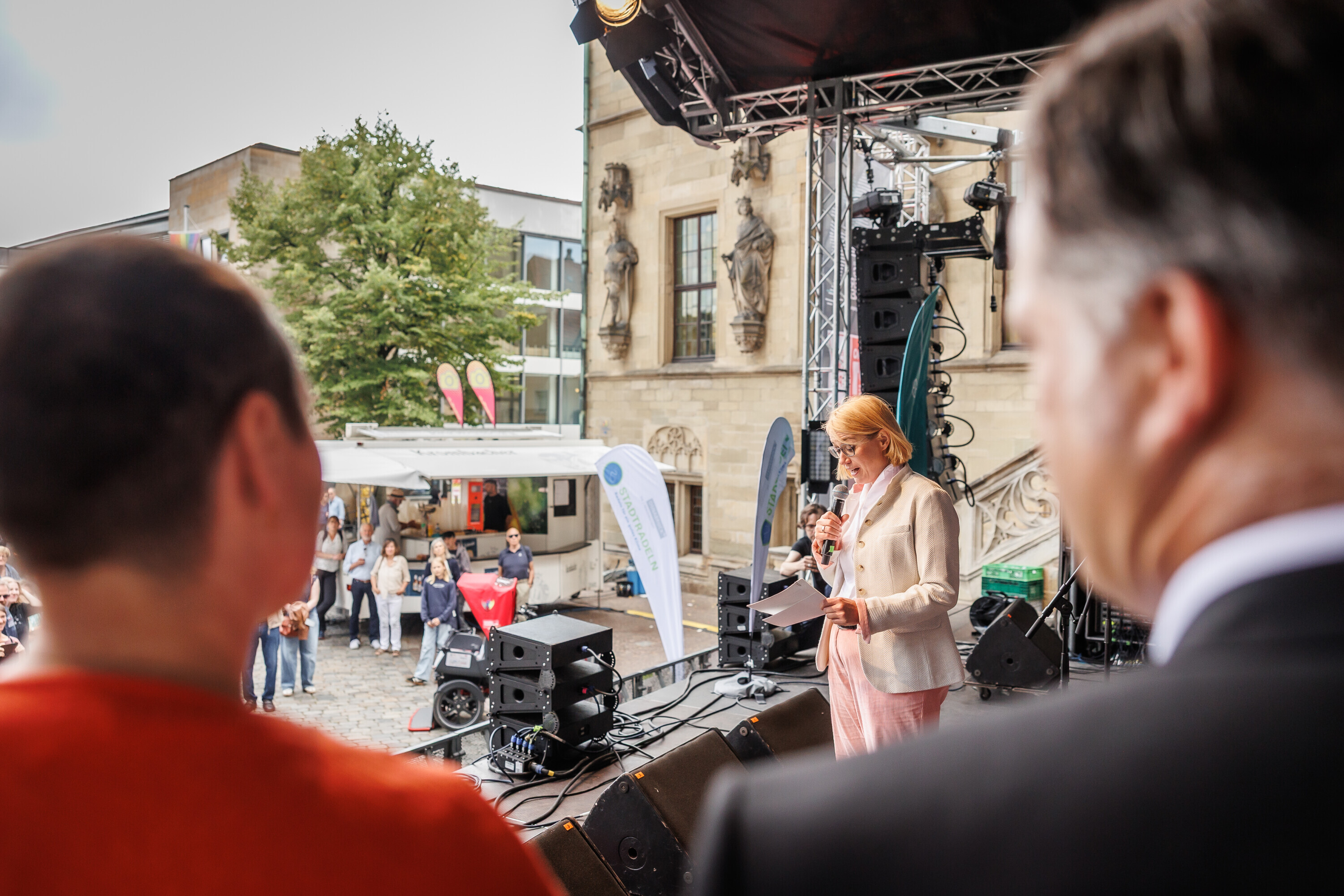 Moderatorin spricht auf der Bühne des Charity Stadtradelns 2025, während zwei Personen im Vordergrund zuhören.