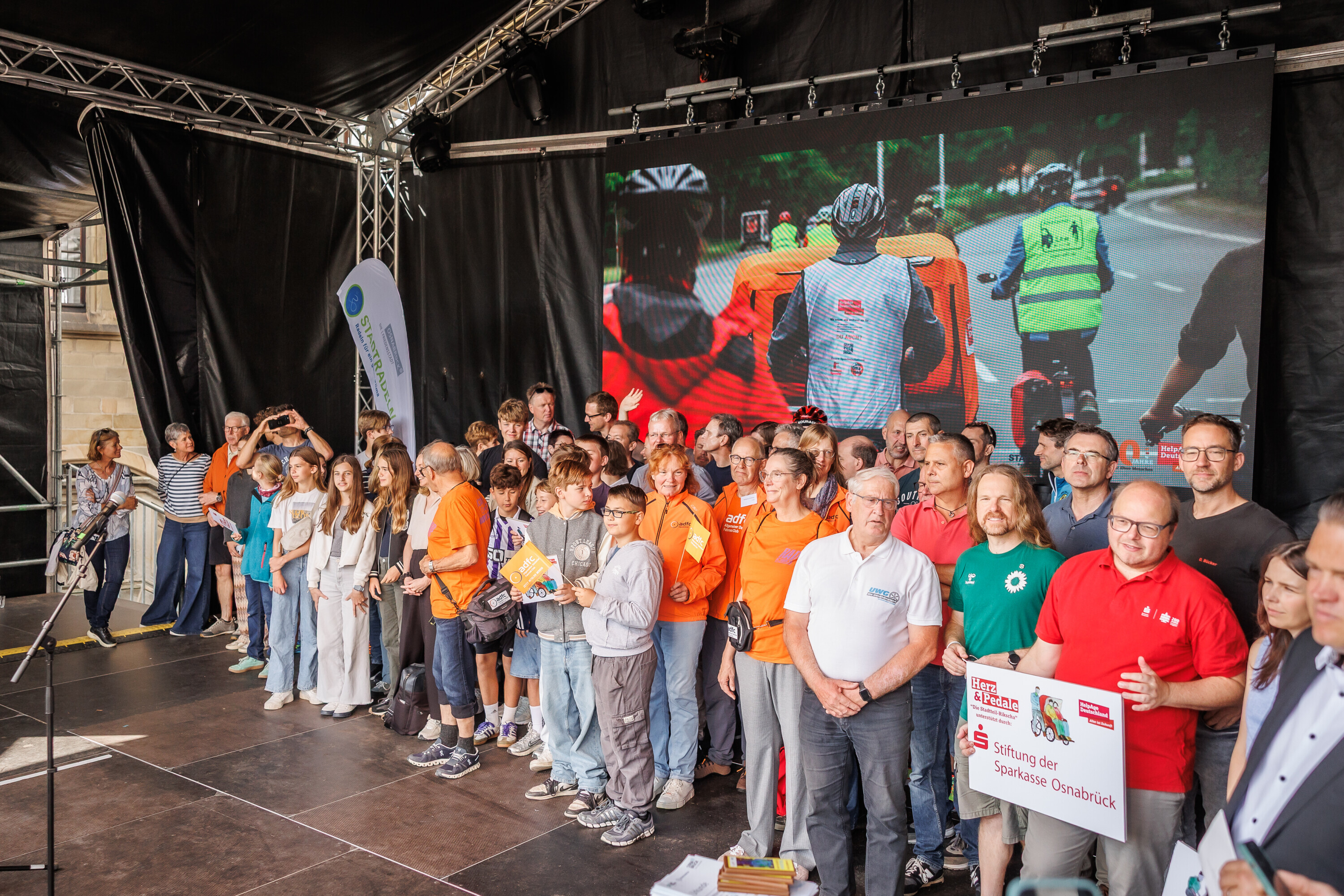 Gruppenfoto aller Preisträgerinnen und Preisträger des Charity Stadtradelns 2025 auf der Bühne mit großem Bildschirm im Hintergrund.